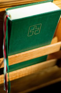 Image of the green Lutheran Book of Worship  held in a rack on the back of a wooden pew