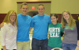 [Image description: five white college-age people stand side-by-side, arms around each other's shoulders. They are smiling at the camera. One woman is wearing a green University of North Texas t-shirt.]