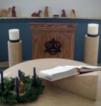 [Image description: photograph of the altar and pulpit of the Anderson Chapel. The Advent wreath is in the bottom left corner of the image. A simple wood nativity set is displayed behind the pulpit.]